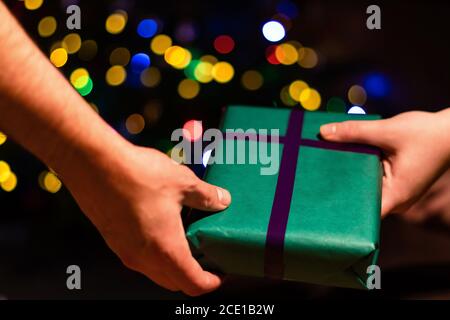 Close up of hands sharing Christmas presents with colourful bokeh balls in the background. Receiving wrapped gifts on holidays Stock Photo