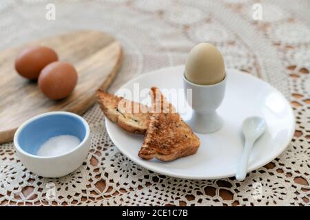 Tasty boiled egg in a cup with crunchy toasted bread for breakfast. Healthy meal on the kitchen table. Stock Photo