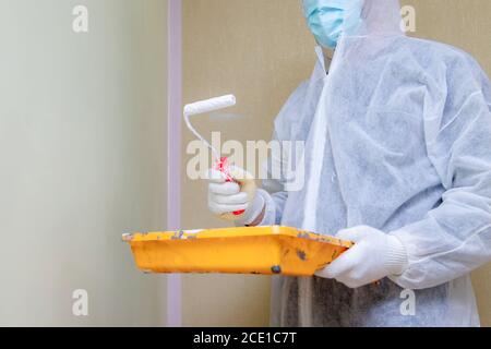 Man in protective work clothes painting the walls white colour with a paint roller. Home renovation project. Apartment renewal concept. Stock Photo