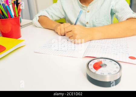 Little boy with lesson timer while doing writing exercise on background Stock Photo