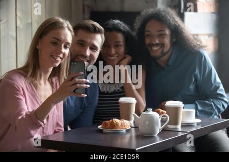 Happy diverse friends taking selfie, sitting at table in cafe Stock Photo