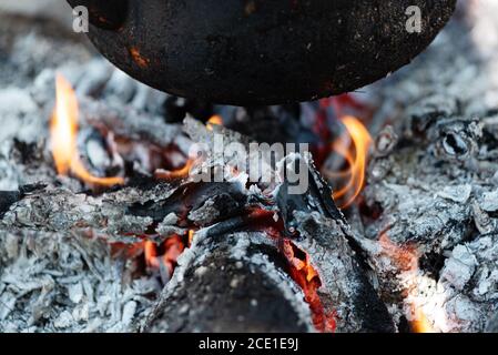 Smoked pot on the embers of the campfire. Food cooked on coals. Summer outdoor activities. Camping family holiday. Selective focus Stock Photo