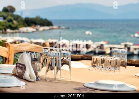 Glasses and plates on a wooden table of a greek tavern over the view of the port of Amaliapoli, Greece Stock Photo