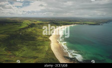 White Beach sand coast aerial zooming, Antrim County, Nortern Ireland. Epic landscape of greenness cliff shore of Atlantic ocean bay. Calm water at dusk cloudy day. Stock Photo