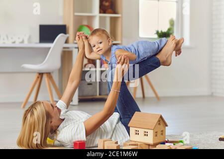 Mom entertains little son by lifting him on his feet up in a bright children's room. Stock Photo
