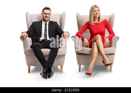 Elegant young man and woman sitting in armchairs isolated on white background Stock Photo