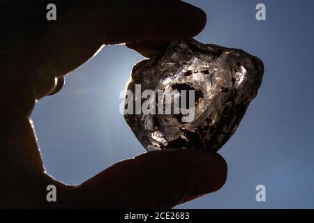 hand is holding a brocken piece of dirty glass against the sun, art Stock Photo