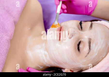 Face peeling mask, spa beauty treatment, skincare. Woman getting facial care by beautician at spa salon, side view, close-up. Anti-aging treatment