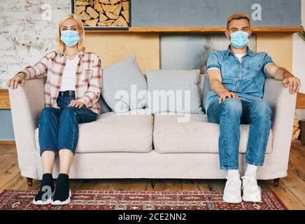 Man and woman in facemask sitting on sofa at home Stock Photo