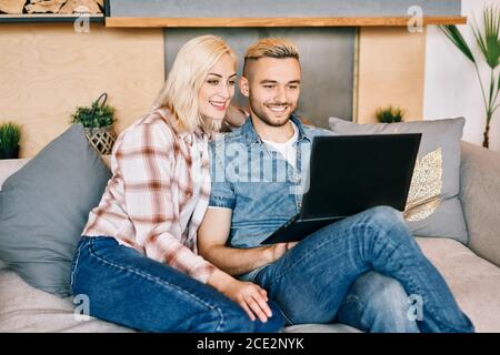 Cheerful young couple with laptop surfing on internet sitting on sofa Stock Photo