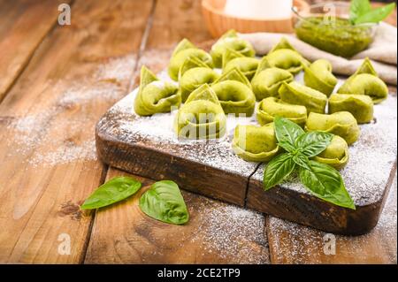 Tortellini e tortelloni typical dishes emilia italy. Food background with homemade raw Italian tortelloni and ingredients for green pesto on wooden background . High angle view. Copy space. Stock Photo