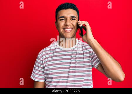 Young arab man having conversation talking on the smartphone looking positive and happy standing and smiling with a confident smile showing teeth Stock Photo