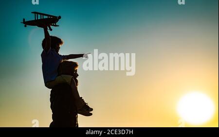 Success and child leader concept. Sunset silhouette of Father and son together. Boy child is sitting on daddy shoulder piggyback while the flight. Stock Photo