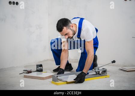 The man in uniform measures the tiles and cuts them with a ceramic saw Stock Photo