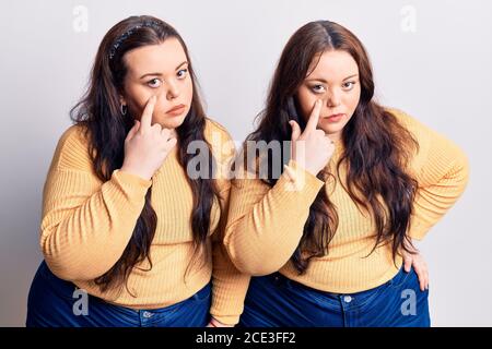Young plus size twins wearing casual clothes pointing to the eye watching you gesture, suspicious expression Stock Photo