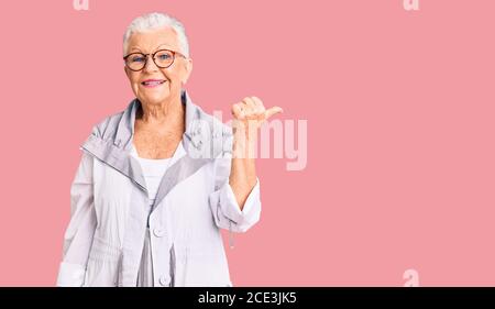 Senior beautiful woman with blue eyes and grey hair wearing casual clothes and glasses smiling with happy face looking and pointing to the side with t Stock Photo