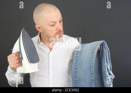 man in a white shirt with an Ironing Flatiron and jeans in his hands Stock Photo