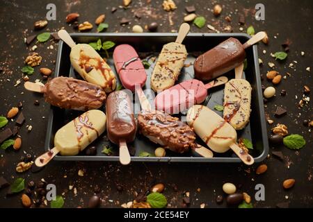 Set of delicious white and milk chocolate and strawberry ice cream on a stick served in metal tray Stock Photo