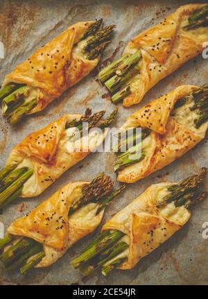 Baked green asparagus in puff pastry sprinkled with sesame seeds. Placed on a white baking paper Stock Photo