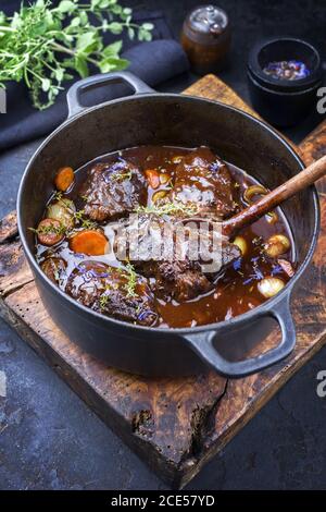 Traditional German braised beef cheeks in brown red wine sauce with carrots and onions offered as closeup in a cast iron Dutch o Stock Photo