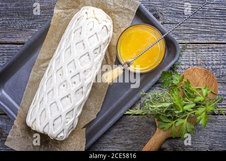 Raw Kassler pork steak as piece in puff pastry and egg yolks as top view offered on a griddle with herbs Stock Photo