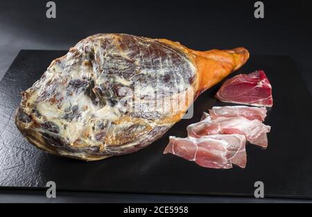 Traditional Spanish jamon Iberico dry aged haunch of a duroc pork as  closeup offered on black background Stock Photo - Alamy