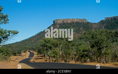 Lords Table Mountain in Peak Range National Park rising into blue sky with road snaking through foreground cloaked in trees in outback  Australia Stock Photo
