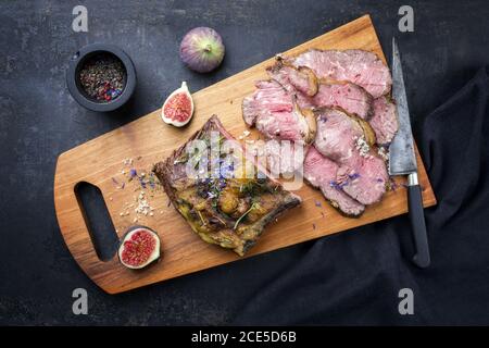 Traditional lunch meat with sliced cold cuts roast beef with gherkin and fig fruit as top view on a modern design cutting board Stock Photo