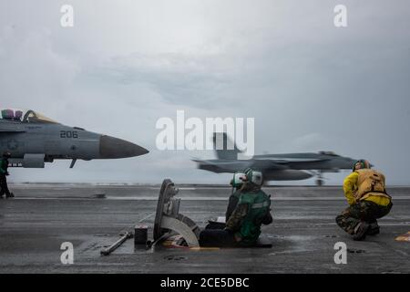 200827-N-ML137-1067 PHILIPPINE SEA (Aug. 27, 2020) Sailors signal to connect an F/A-18E Super Hornet attached to the Royal Maces of Strike Fighter Squadron (VFA) 27 to a catapult while an F/A-18E Super Hornet launches from the flight deck of the Navy’s only forward-deployed aircraft carrier USS Ronald Reagan (CVN 76). Ronald Reagan, the flagship of Carrier Strike Group 5, provides a combat-ready force that protects and defends the United States, as well as the collective maritime interests of its allies and partners in the Indo-Pacific region. (U.S. Navy photo by Mass Communication Specialist Stock Photo