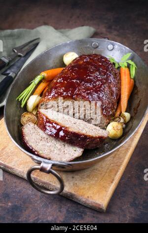 Traditional American meatloaf with ketchup from ground beef with carrots and onion as closeup in a copper saucepan