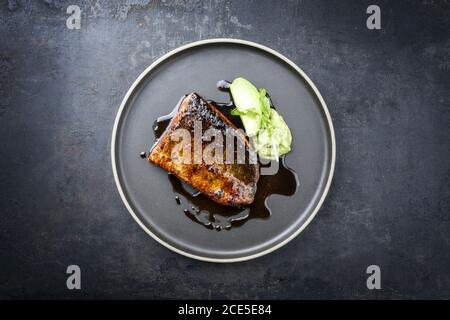 Minimalistic design Japanese salmon fish filet with avocado and wasabi creme glazed in teriyaki sauce as closeup on a modern des Stock Photo