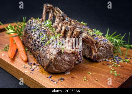 Barbecue rack of lamb with carrot and herbs offered as closeup on a modern design wooden board Stock Photo