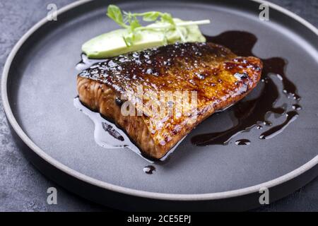 Minimalistic design Japanese salmon fish filet with avocado and wasabi creme glazed in teriyaki sauce as closeup on a modern des Stock Photo