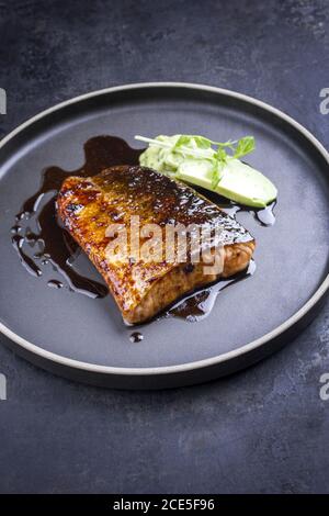 Minimalistic design Japanese salmon fish filet with avocado and wasabi creme glazed in teriyaki sauce as closeup on a modern des Stock Photo