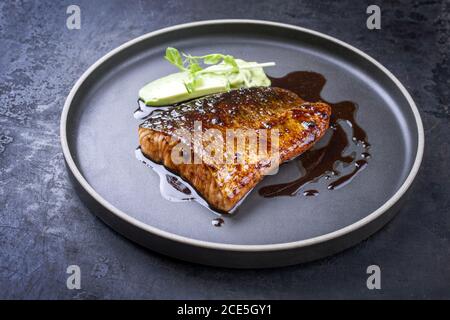 Minimalistic design Japanese salmon fish filet with avocado and wasabi creme glazed in teriyaki sauce as closeup on a modern des Stock Photo
