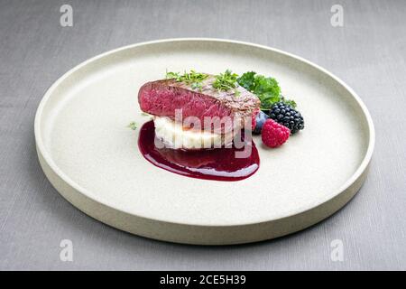 Fried dry aged venison tenderloin fillet medallion steak natural with mashed potatoes and raspberry sauce as closeup on a modern Stock Photo
