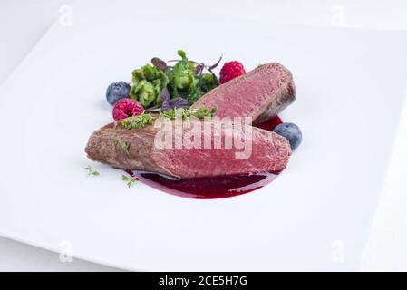 Fried dry aged venison tenderloin fillet medallion steak natural with kalette and raspberry sauce as closeup on a modern design Stock Photo