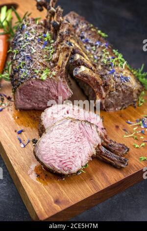 Barbecue rack of lamb with carrot and herbs offered as closeup on a modern design wooden board Stock Photo