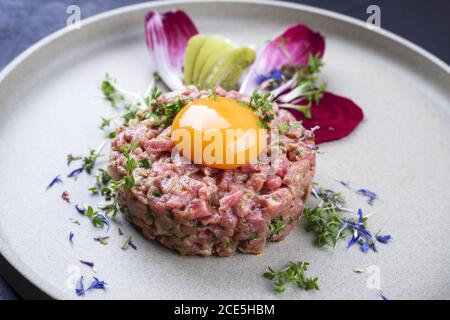 Gourmet tartar raw from beef fillet with yellow of the egg and vegetable as closeup on modern design dish Stock Photo