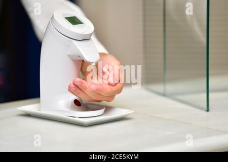 Close up of a male hand using an automatic hydroalcoholic gel dispenser on an out of focus background. Hygiene and safety concept. Stock Photo