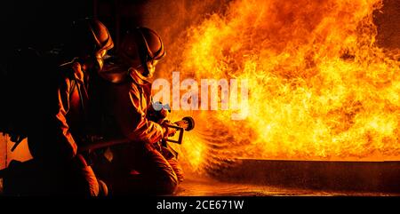 Firefighters use twirl water fog spraying down fire flame. Stock Photo
