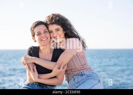 Two female friends hugging by the beach Stock Photo
