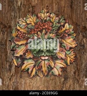 Highly decorative concrete garden art, face of autumn leaves of Green Man, British mythical spirit of the forests, on background of brown tree bark Stock Photo