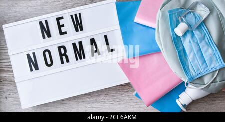 Lightbox with text NEW NORMAL protective face mask and sanitizer. Back to school. Books falling from backpack. Social distancing Stock Photo