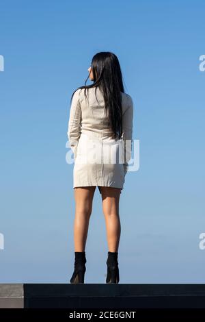 Young woman wearing a short dress, pantyhose and high heels posing on a ...