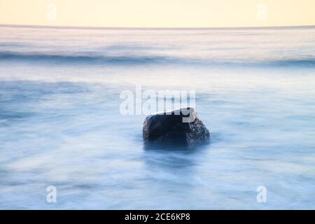 Romantic atmosphere in peaceful morning at sea. Big boulders sticking out from smooth wavy sea. Pink horizon Stock Photo
