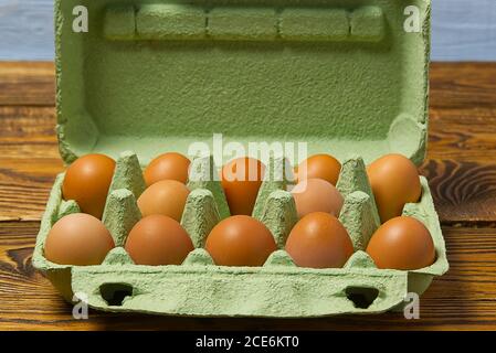 Dozen eggs in green cardboard package on wooden table closeup. Stock Photo