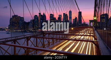 Brooklyn Bridge with light trails and view on Lower Manhattan skyscrapers at Dusk. Evening in New York City, NY, USA Stock Photo