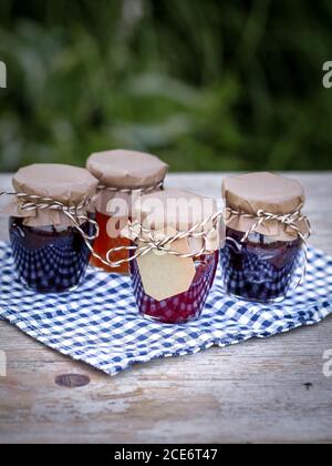 Four jars with homemade jam from blackberries, strawberries and apricots on the table in the garden. Close up with copy space.  Stock Photo