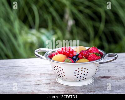 Four jars with homemade jam from blackberries, strawberries and apricots on the table in the garden. Bowl of fresh fruits on the background. Stock Photo